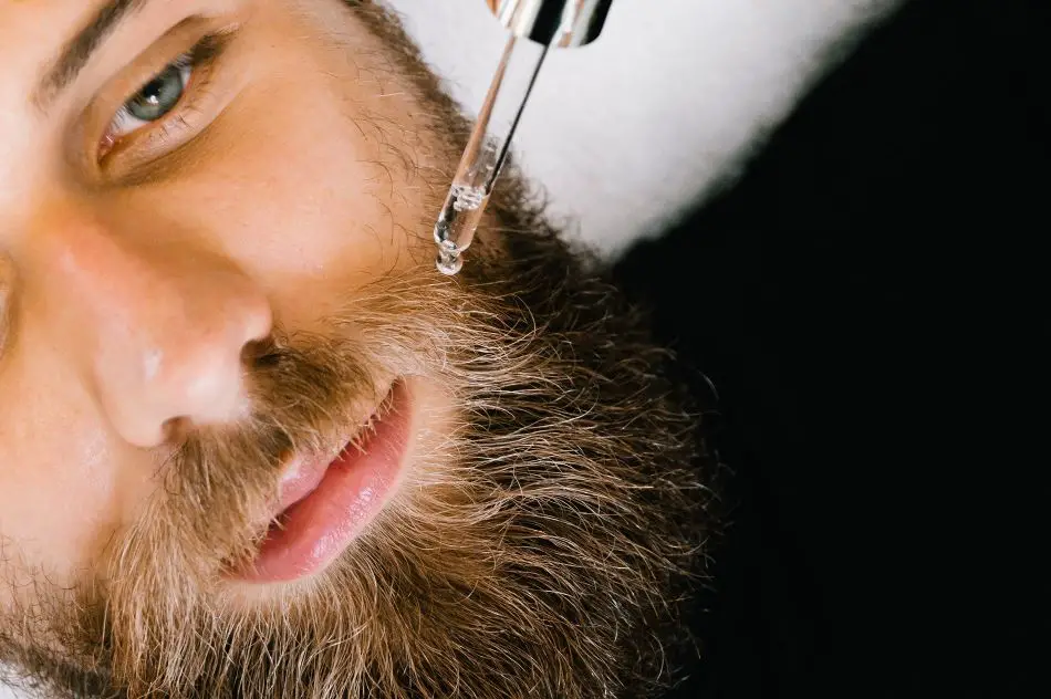 a man applying jojoba oil on his beard through pipet - jojoba oil for beard