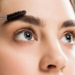 woman applying coconut oil on eyebrows with a spoolie - coconut oil for eyebrows