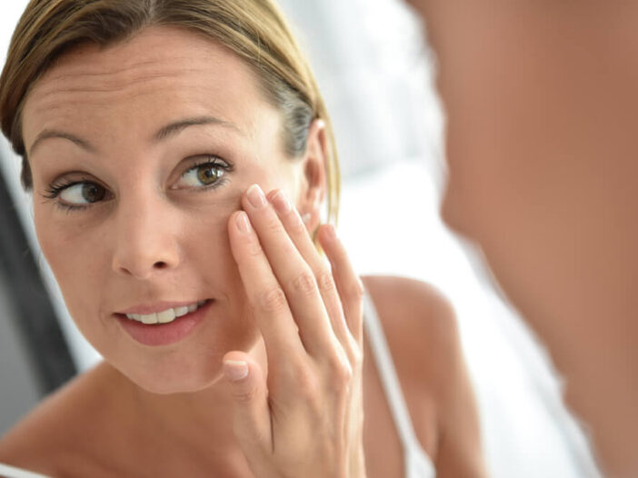 woman looking at her face in the mirror - coconut oil for wrinkles