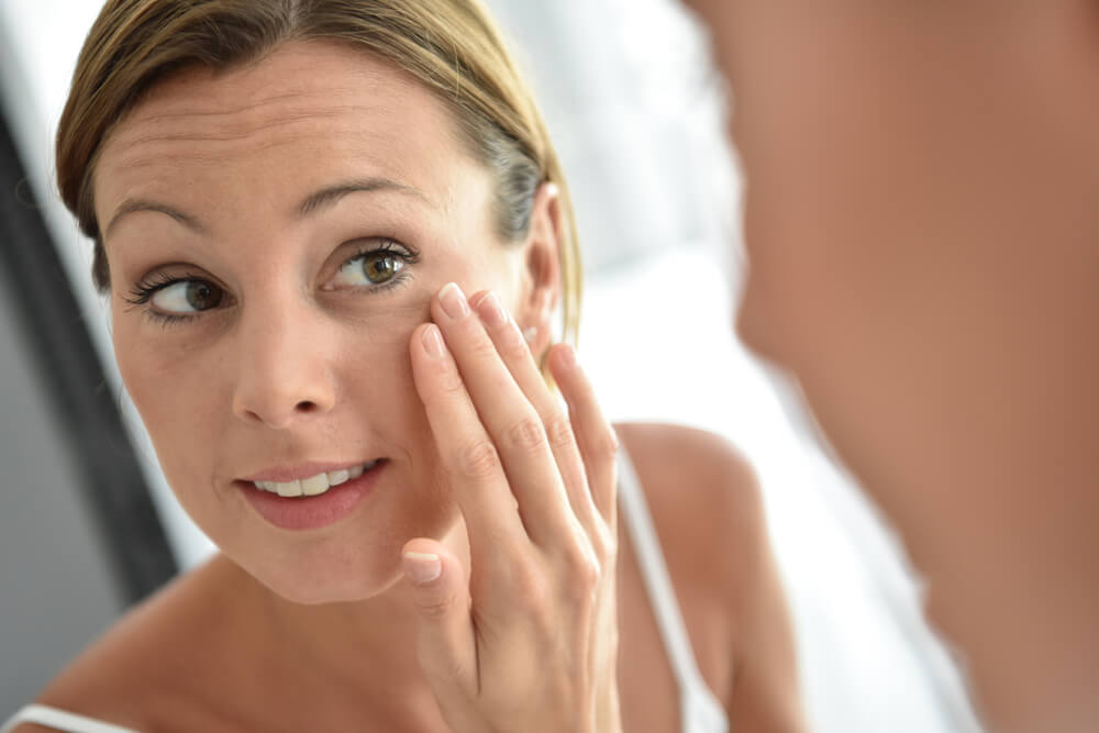woman looking at her face in the mirror - coconut oil for wrinkles 